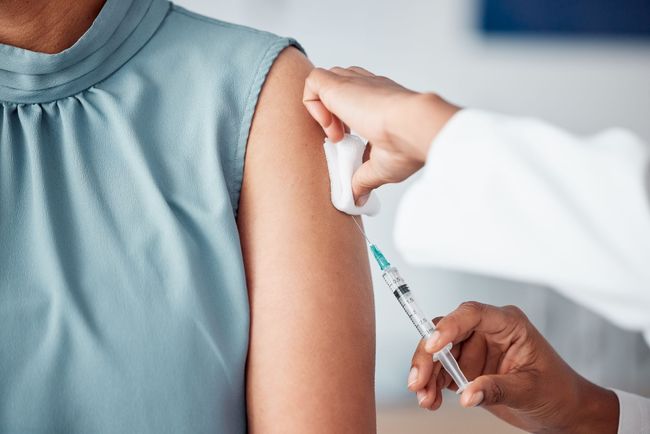 Personne recevant une injection dans le haut du bras ; professionnel de santé administrant un vaccin.