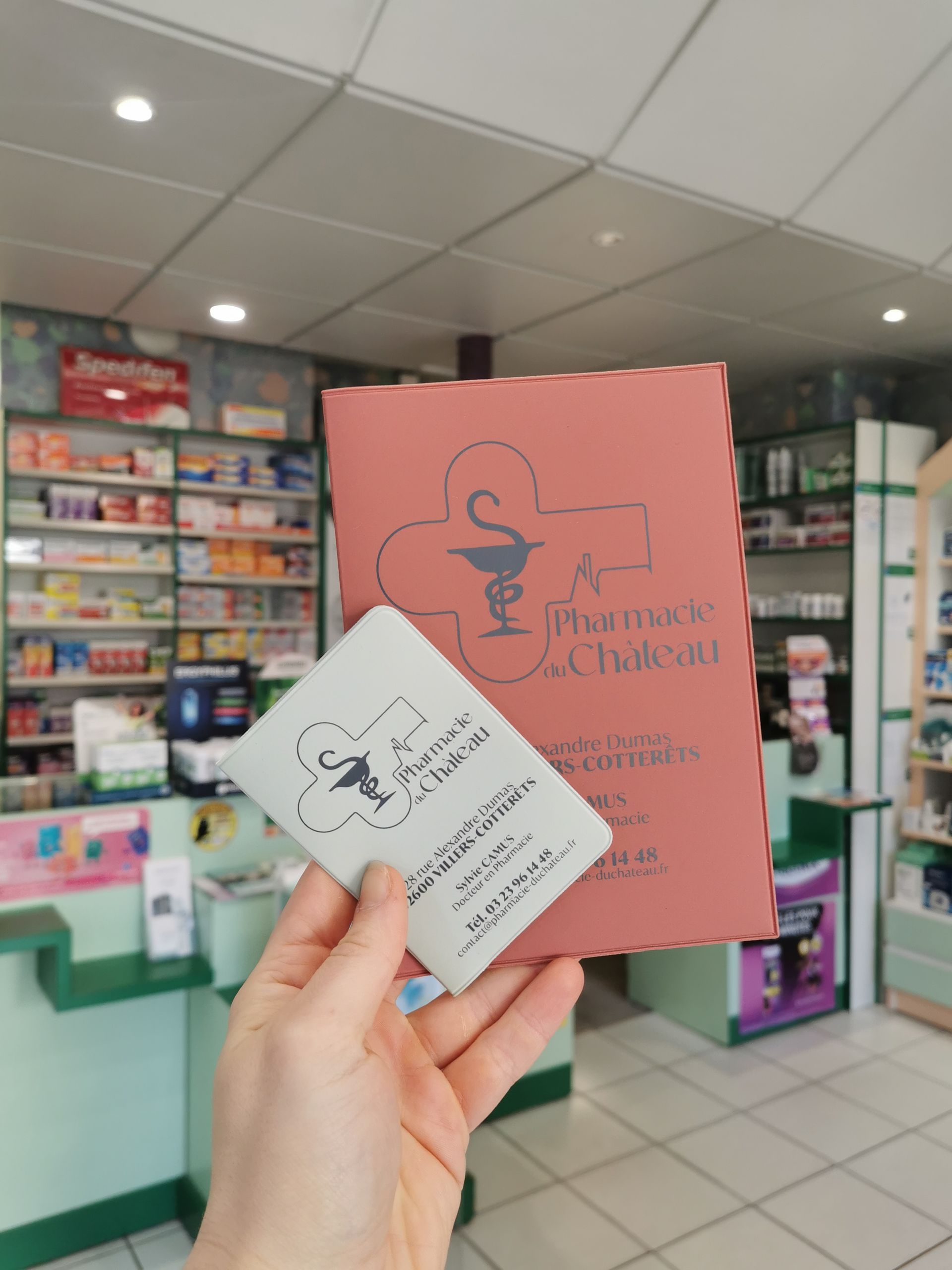 Une main tient une carte blanche et un dépliant rose.