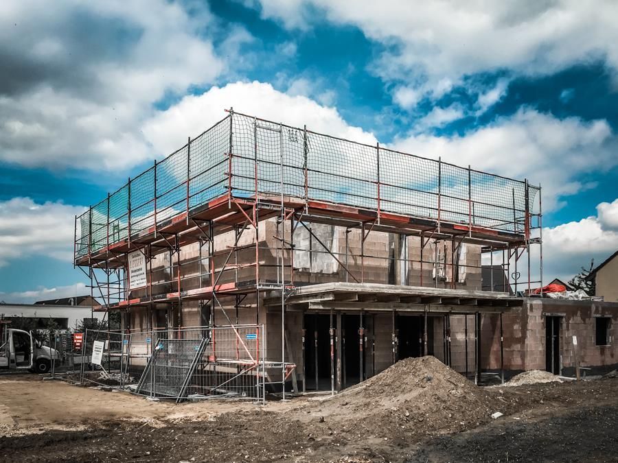 Ein Haus wird gebaut, mit Gerüsten und einem blauen Himmel im Hintergrund.