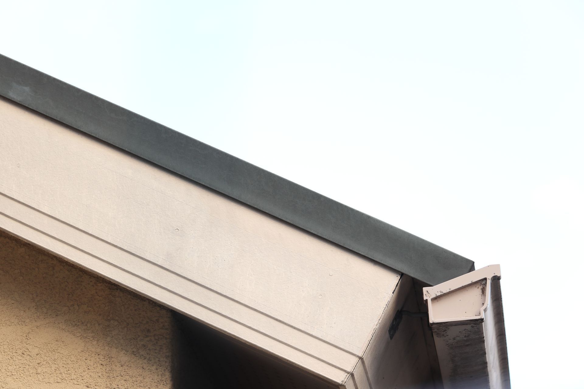 Gros plan sur le bord d'un toit de maison avec une corniche et une gouttière beige sur un ciel pâle.