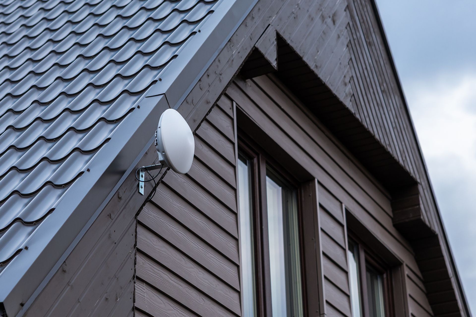 Façade, couverture et bardage sur une maison gris foncé, vue sur une antenne parabolique et deux fenêtres.