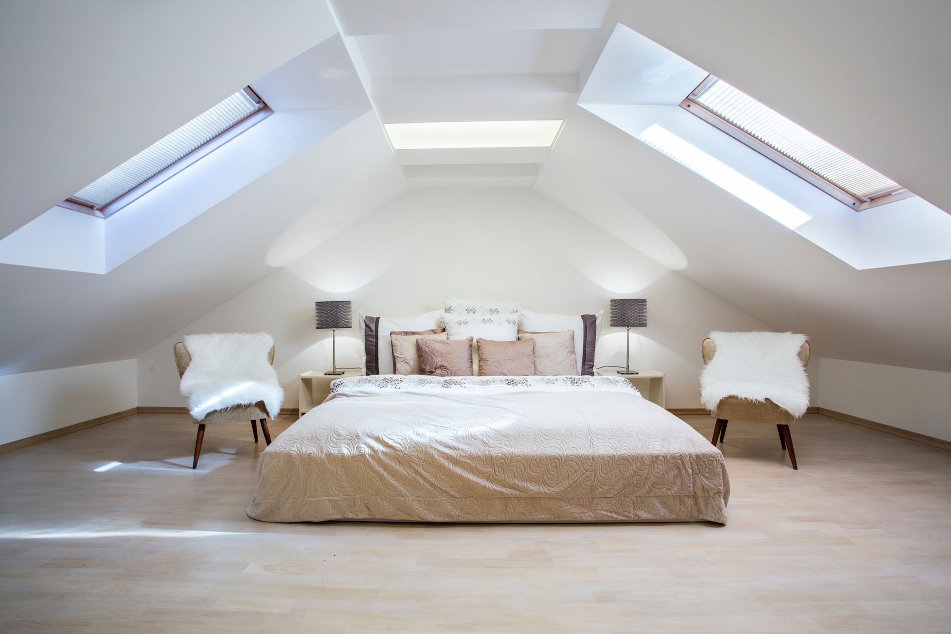 Chambre mansardée lumineuse avec un grand lit, deux chaises et des fenêtres de toit des deux côtés.