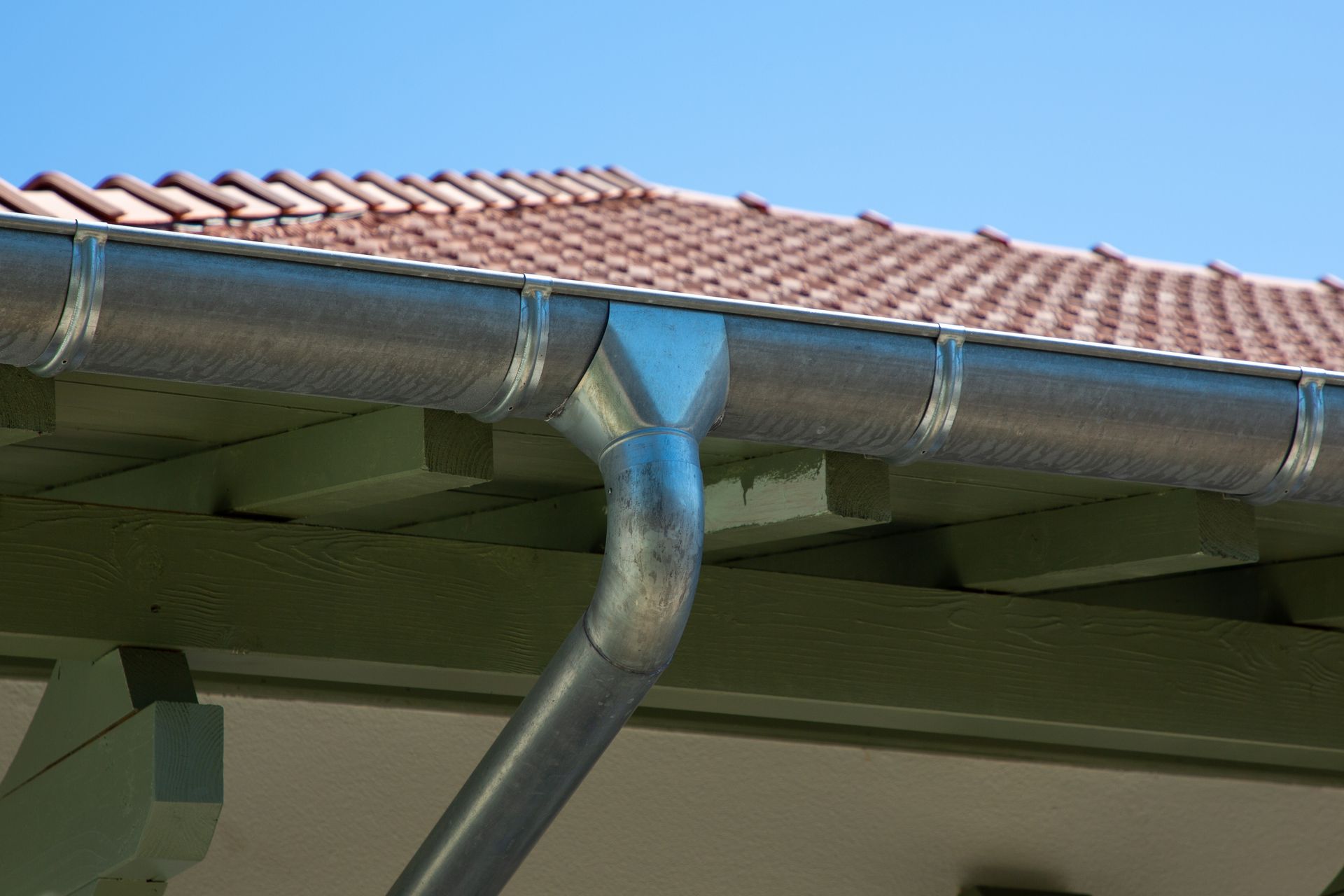 Gouttière et descente d'eau en zinc sur le toit d'une maison aux tuiles rouges.