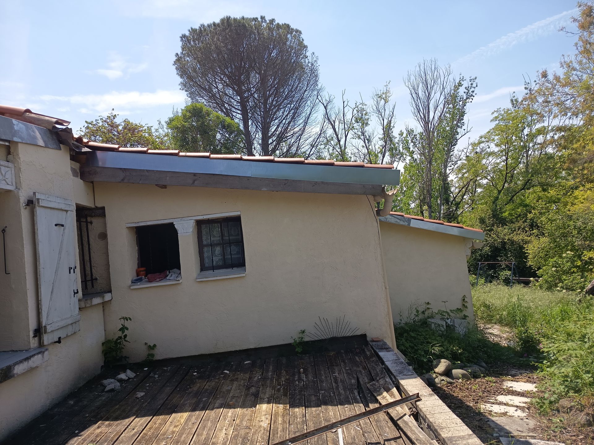 Petit bâtiment couleur crème avec un toit en pente avec un habillage en zinc, vue sur une terrasse en bois.