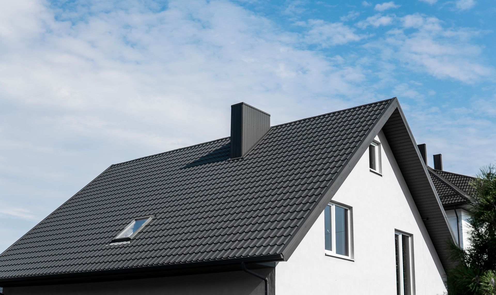 Maison avec un toit de tuiles gris foncé et un puits de lumière sous un ciel bleu.