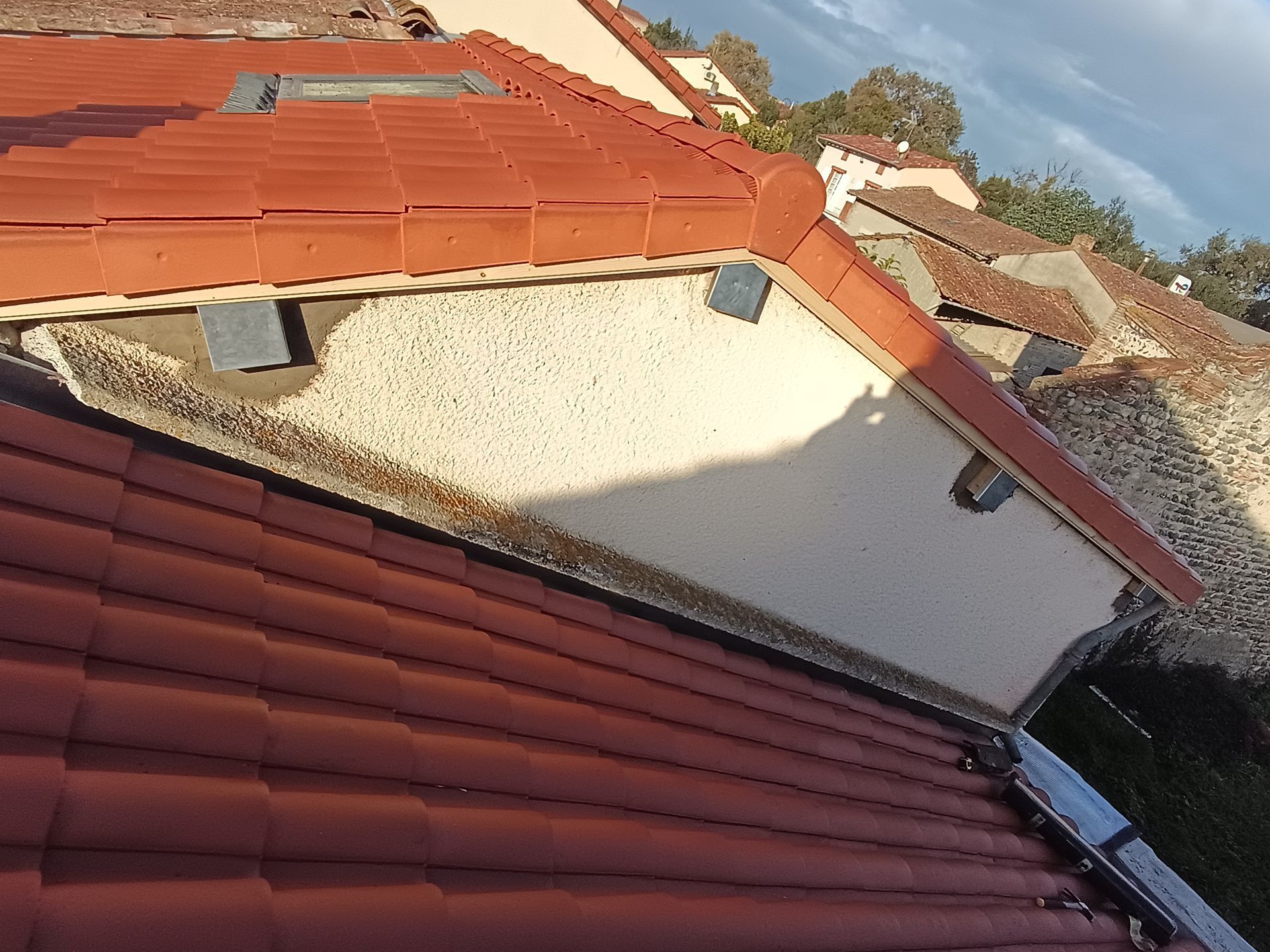 Toits de tuiles rouges, murs en stuc crème et toit en pente baigné de soleil sous un ciel bleu.