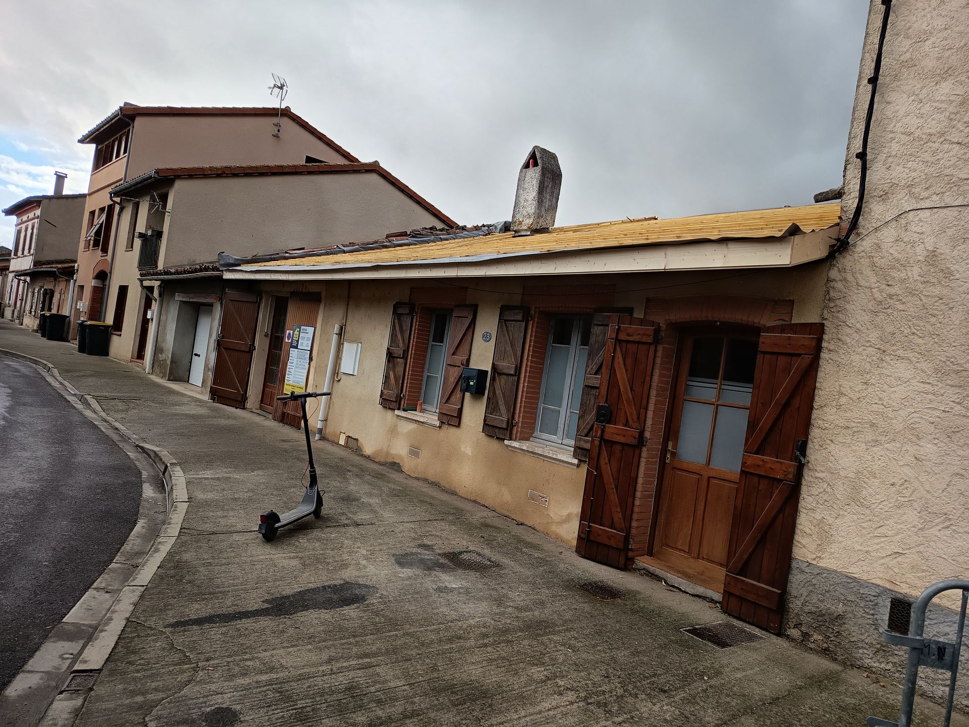 Rue tranquille bordée de maisons aux portes en bois, avec une trottinette garée sur le trottoir.