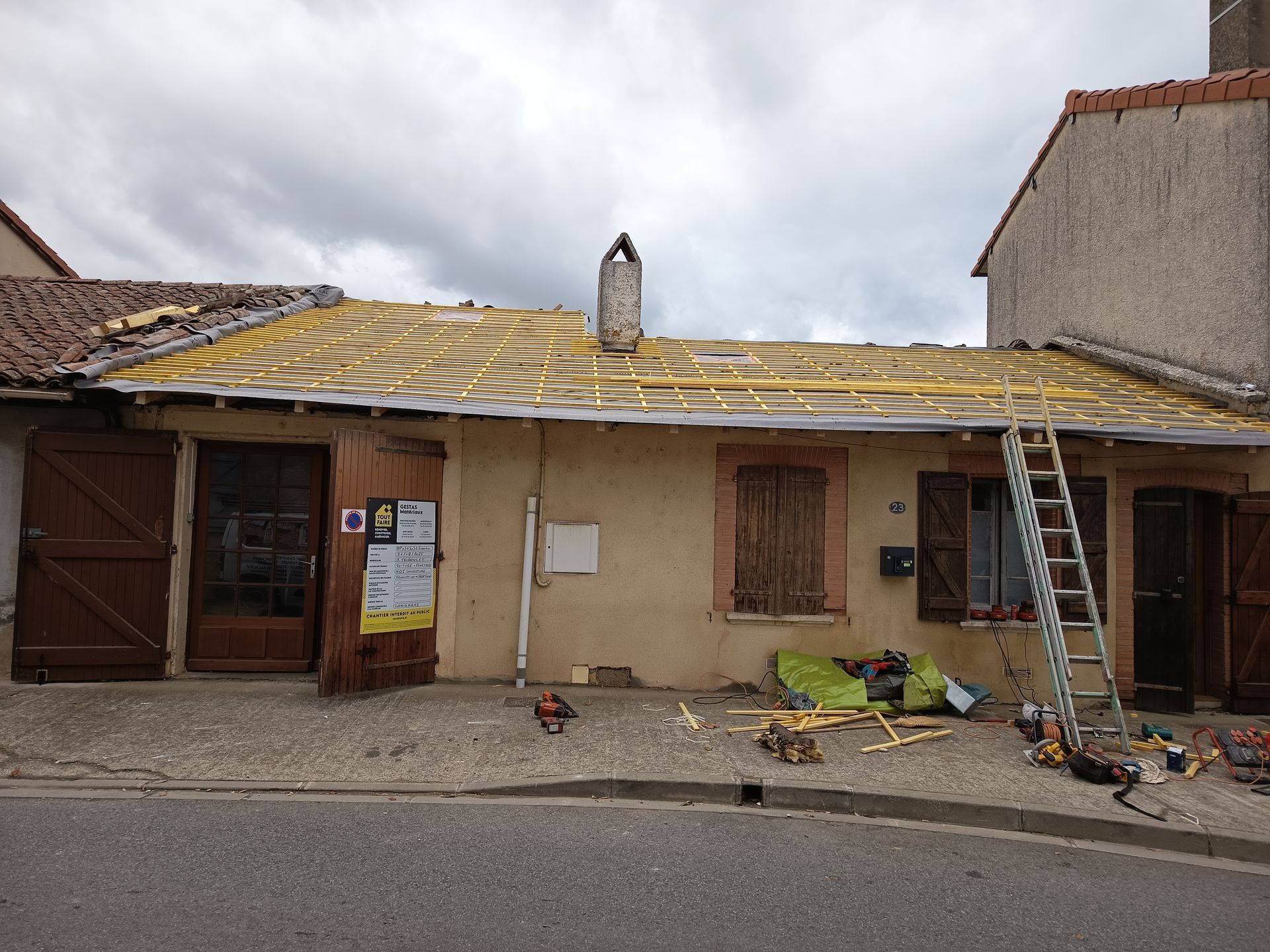 Maison en cours de rénovation, une échelle et des débris éparpillés sur le devant de la maison.