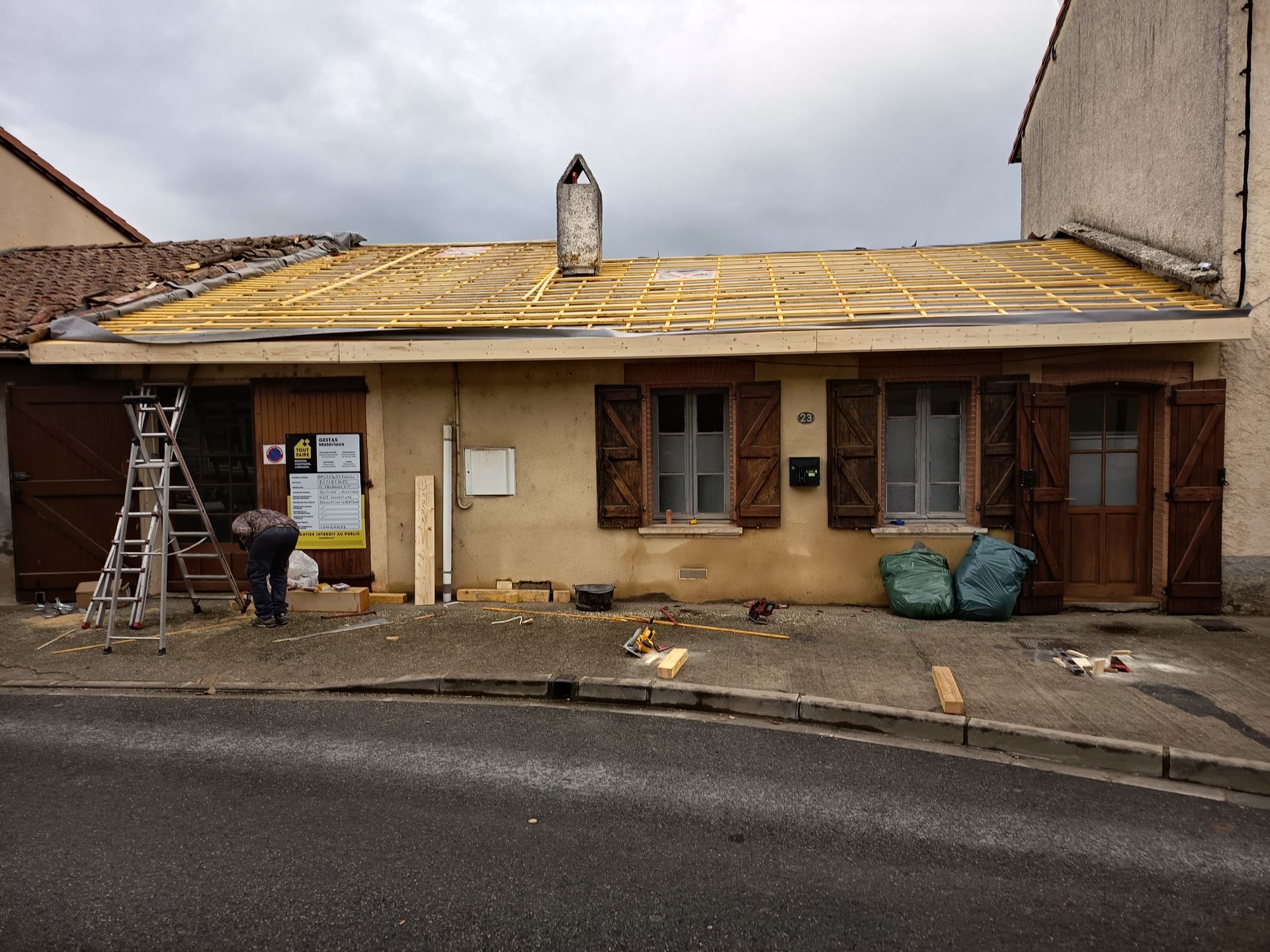 Façade de maison en cours de rénovation, débris et échelle posés sur un sol mouillé.