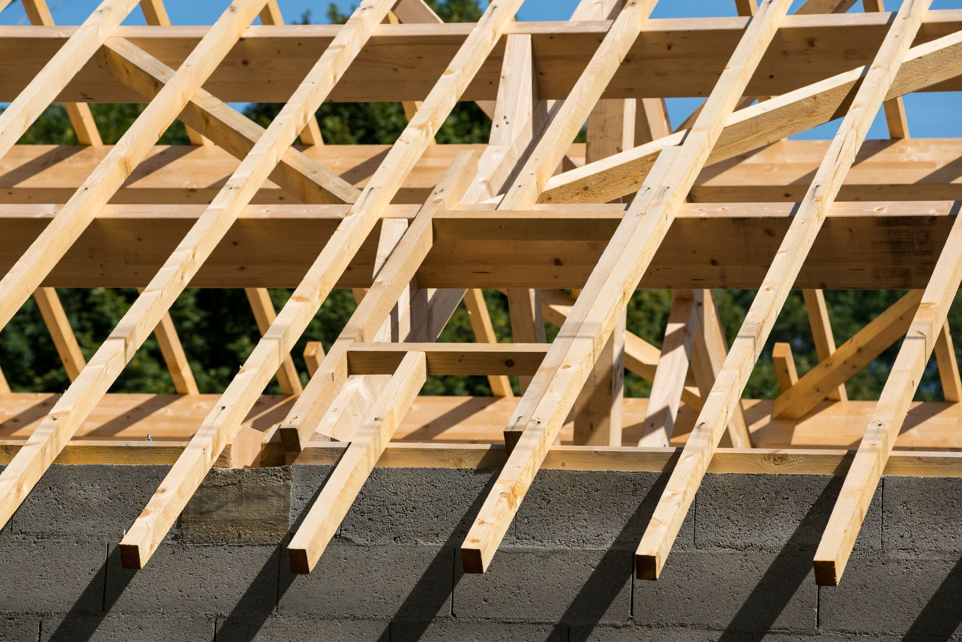 Charpente de toit en bois en construction sur une ossature de bâtiment, avec des murs en bloc de béton en dessous.