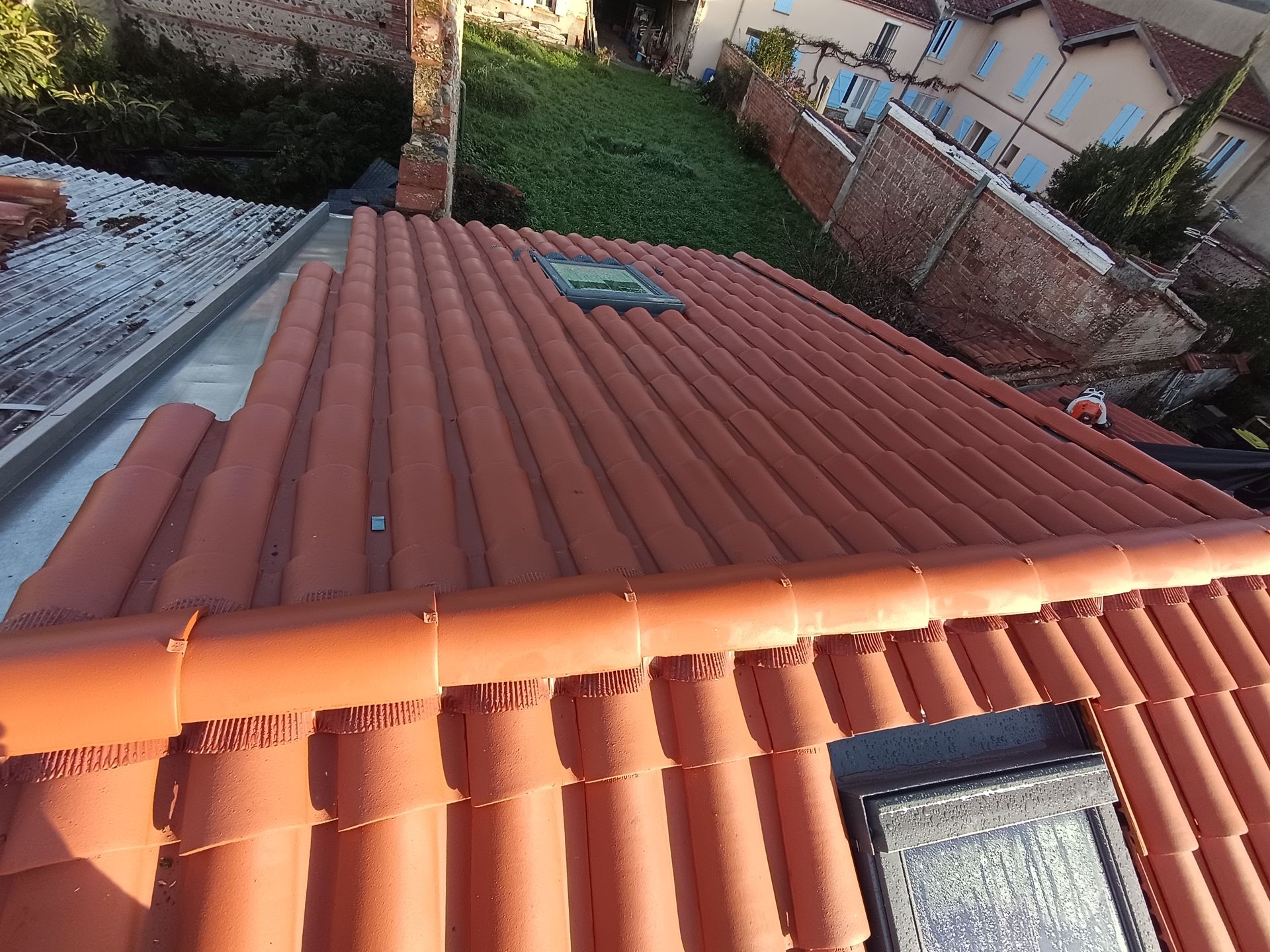 Toit recouvert de tuiles en terre cuite rouge avec un puits de lumière, vue d'en haut dans un quartier résidentiel.