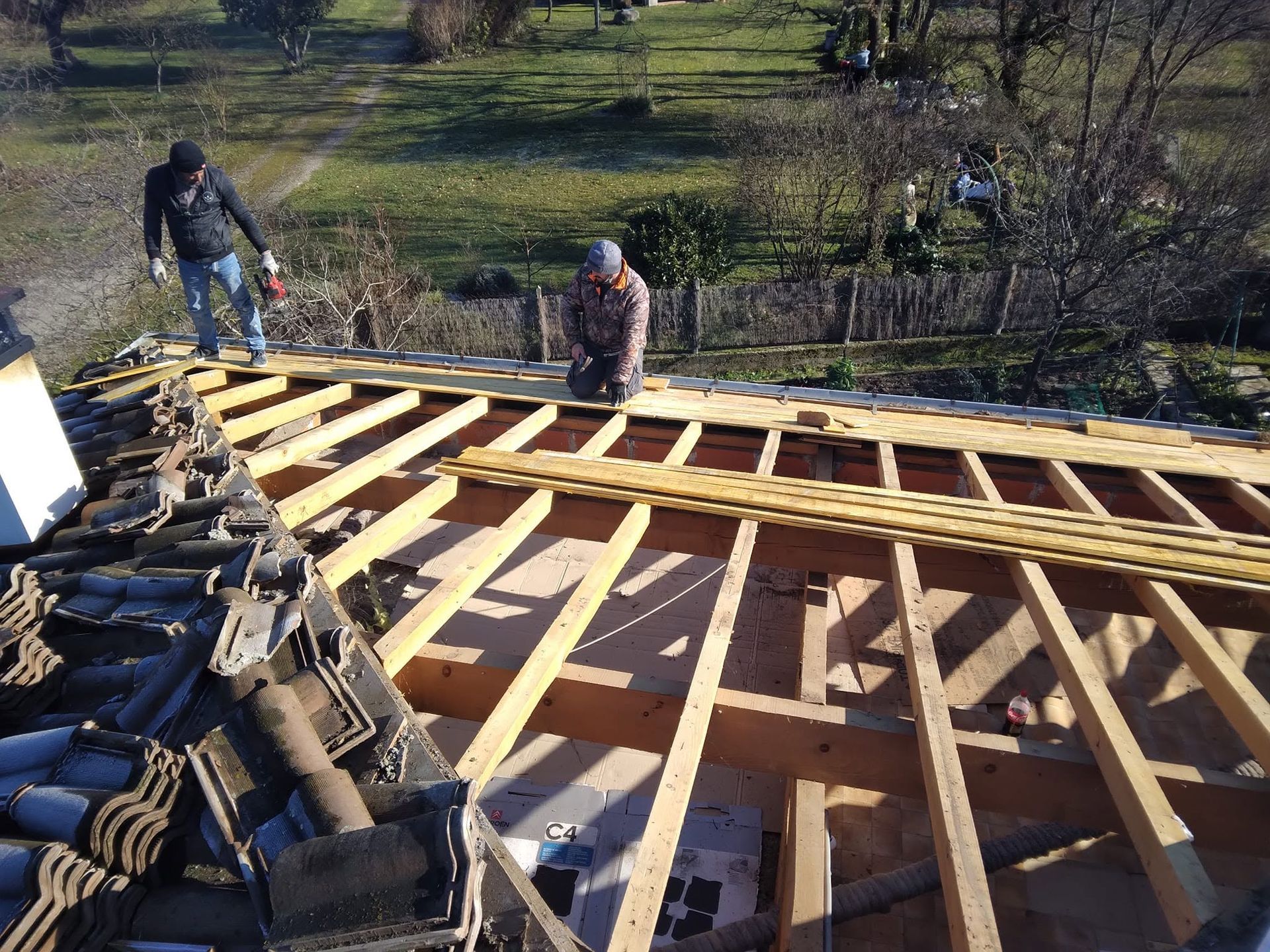 Des couvreurs installent des chevrons en bois sur le toit d'une maison, avec des tuiles empilées au premier plan.