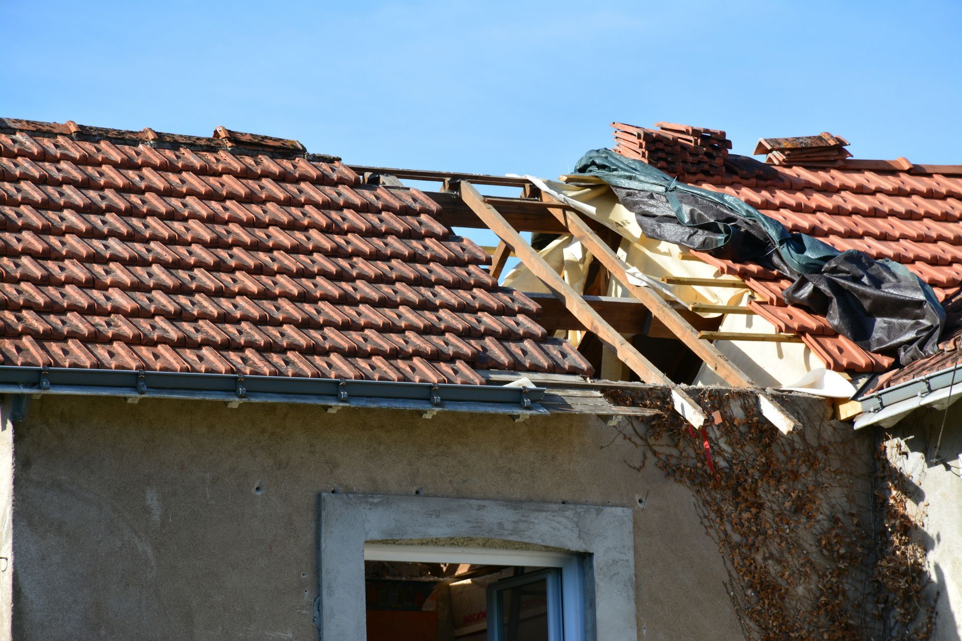 Toiture d'une maison en cours de rénovation, avec chevrons apparents et tuiles manquantes.