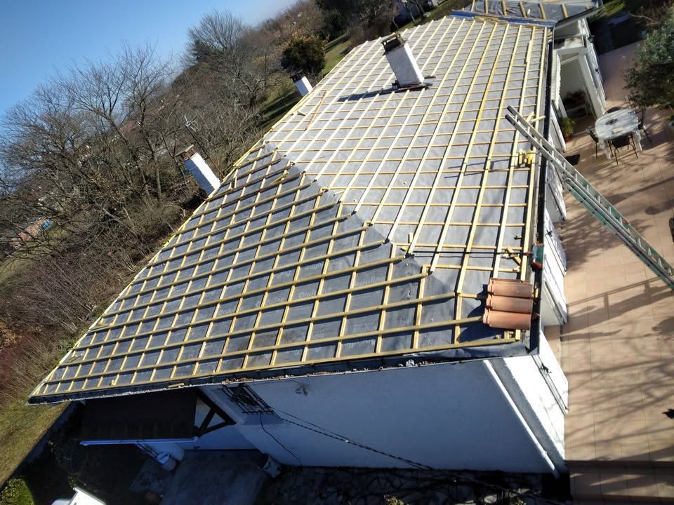 Travaux en cours sur un toit de bâtiment à côté d'arbres et d'une allée.