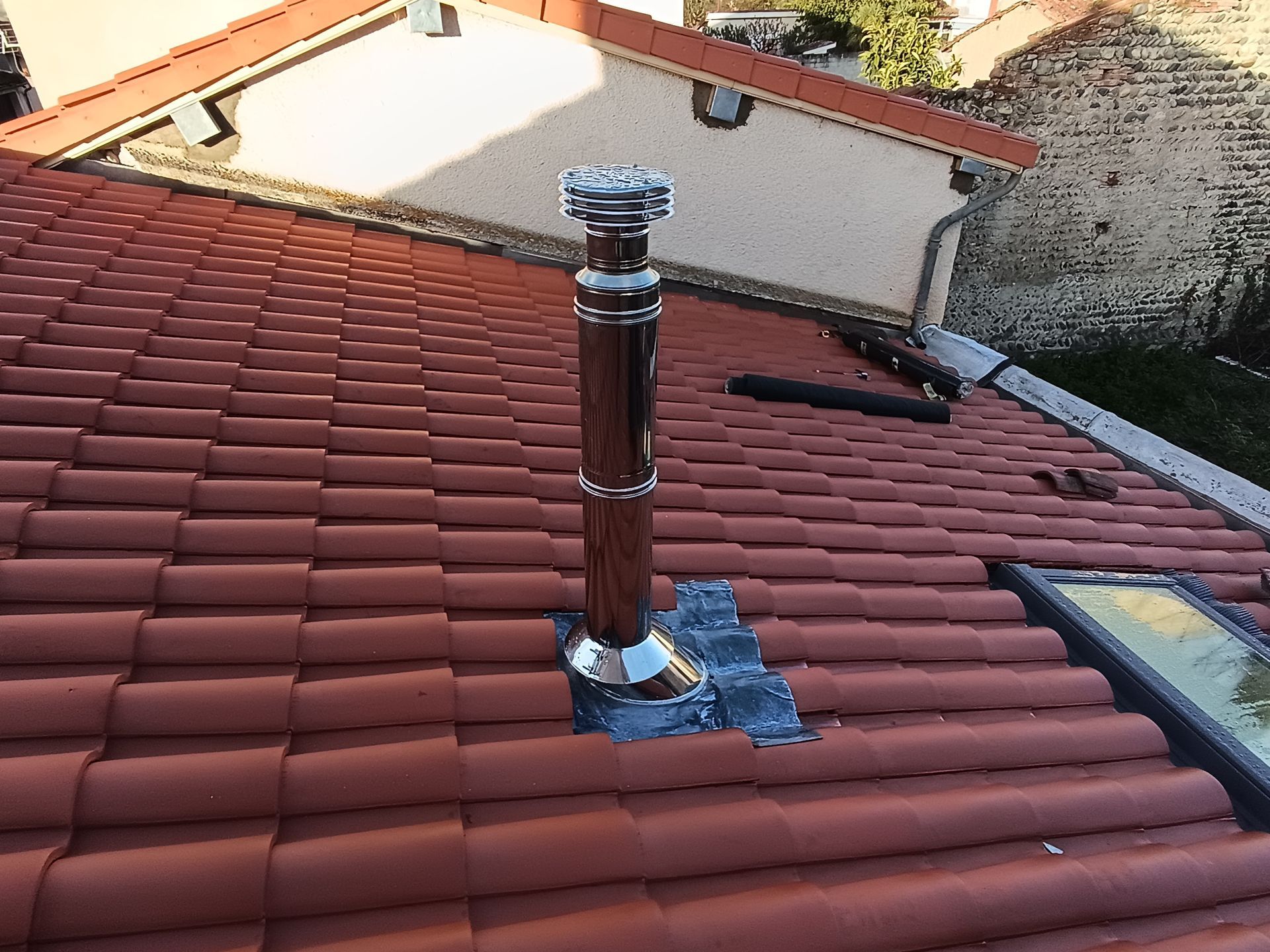 Tuyau de ventilation de toit sur toiture en tuiles rouges avec un solin en zinc.