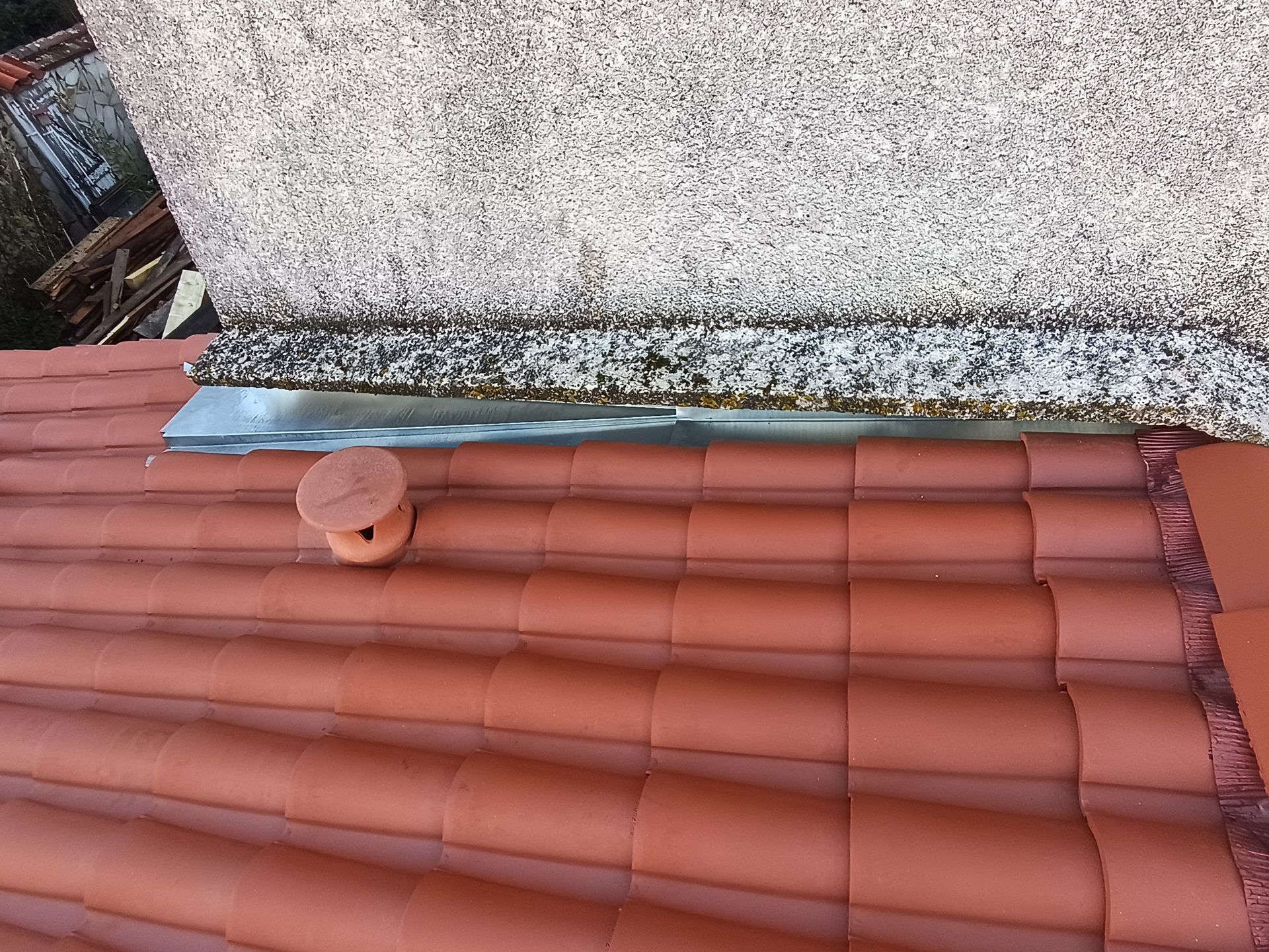 Tuiles de terre cuite rouge à côté d'un mur de pierre avec une sortie d'aération.