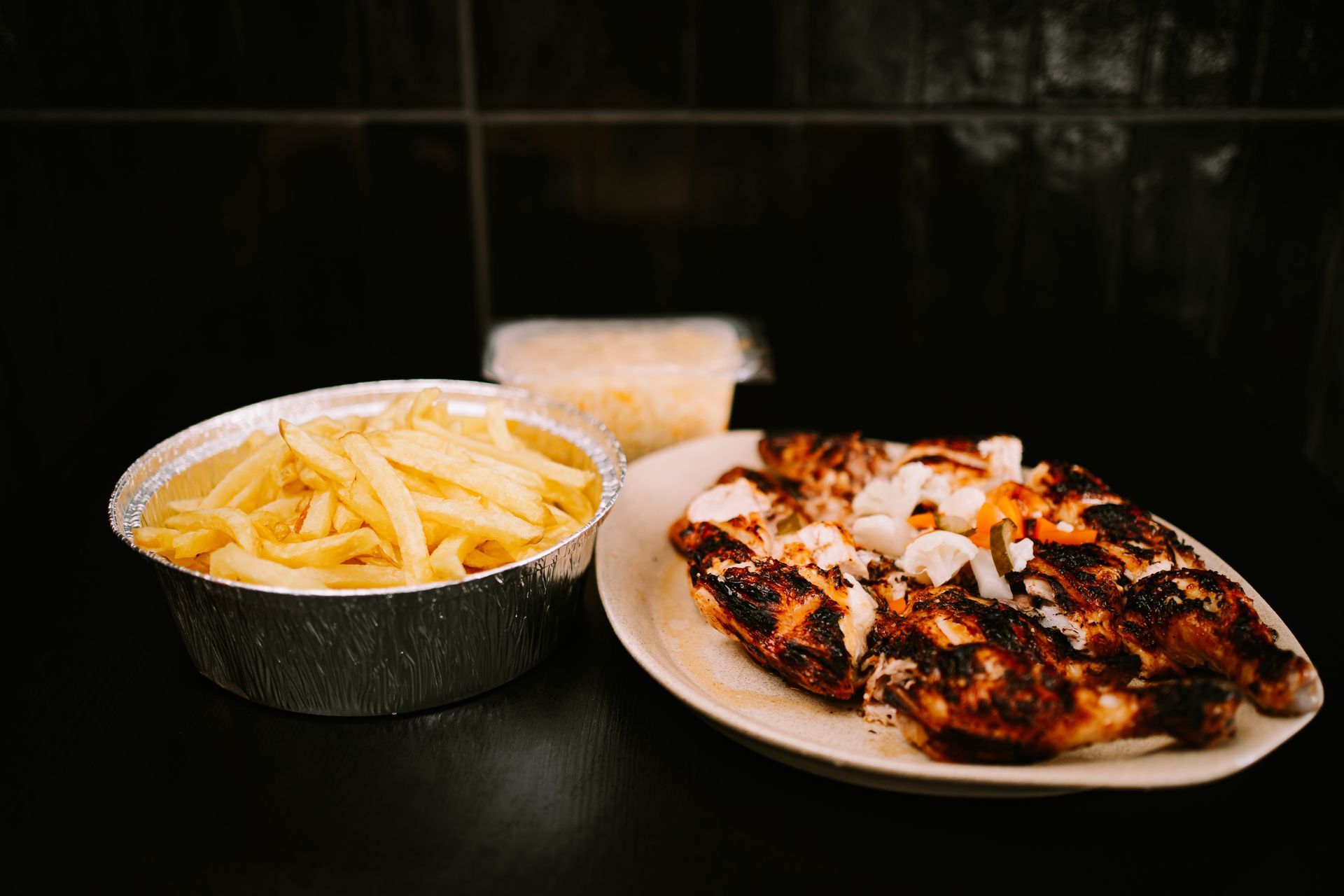 Frango grelhado, batatas fritas e salada de repolho sobre uma superfície escura.