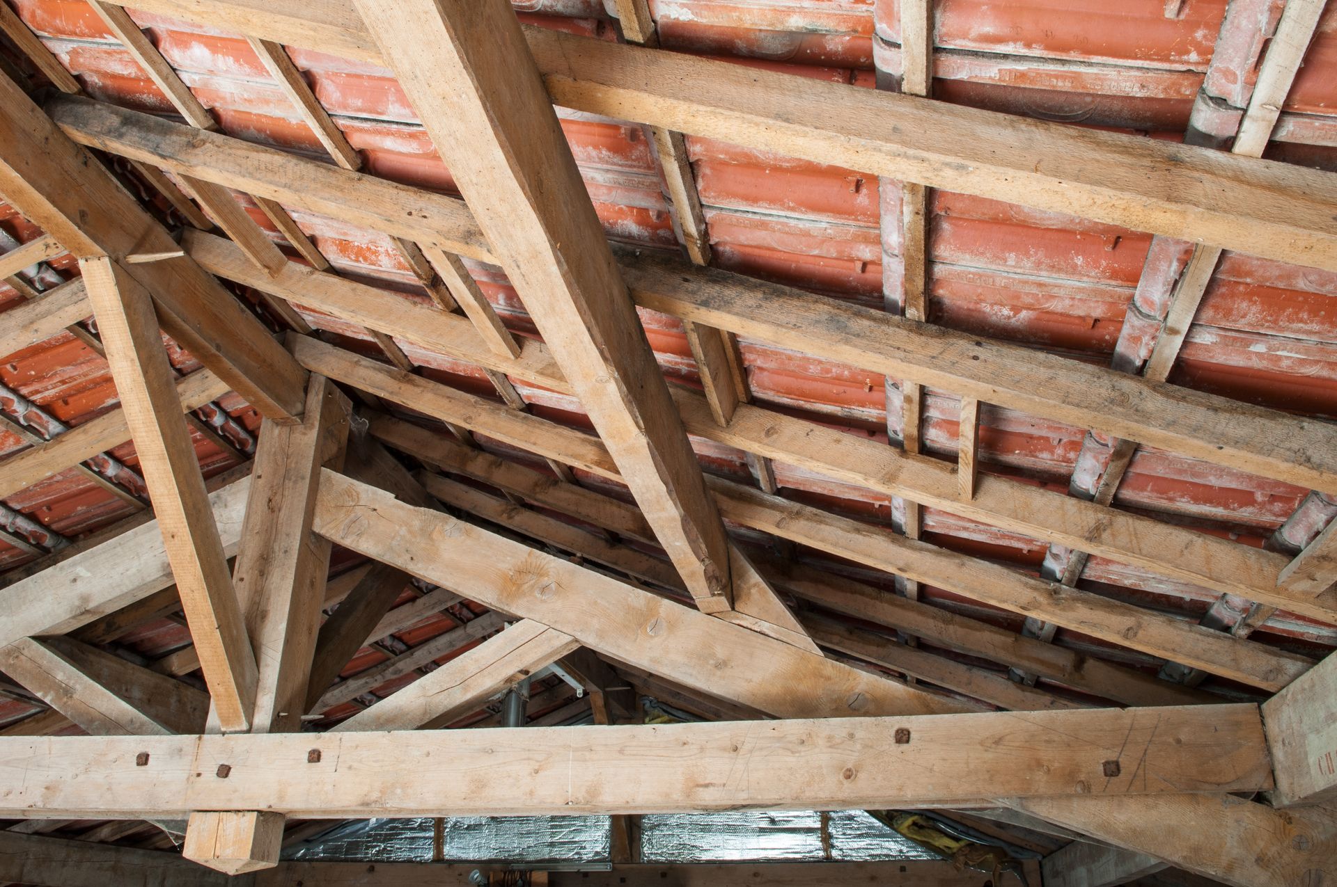 Une charpente de toit en bois soutenant des tuiles de terre cuite rouge, vue de l'intérieur d'un grenier.
