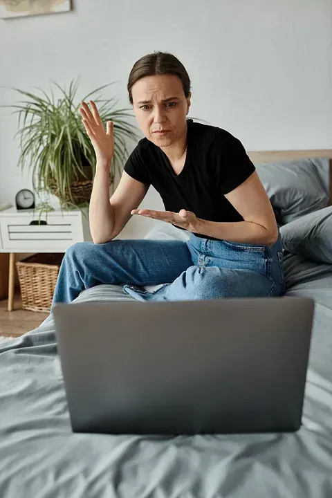 Una mujer está sentada en una cama mirando una computadora portátil.