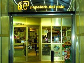 Entrada iluminada de la librería por la noche, con puertas de cristal y letrero amarillo de “papelera del espada”.