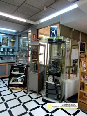 Tienda de electrónica interior con vitrinas de cristal y suelo de baldosas a cuadros blancas y negras.