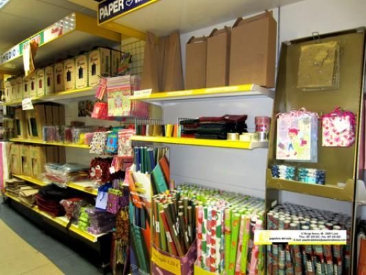 Pasillo de la tienda con estantes llenos de coloridas tarjetas de felicitación, bolsas de regalo y artículos de papel.
