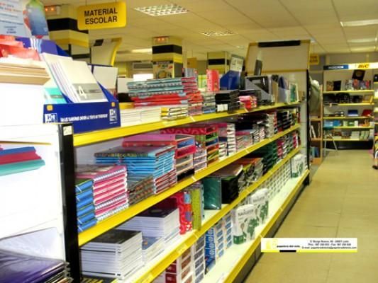 En una tienda, un pasillo de material escolar con cuadernos, carpetas y archivadores de colores en los estantes.