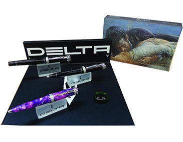 Tres plumas estilográficas de la marca Delta sobre un soporte negro con un pequeño cuadro de paisaje detrás.