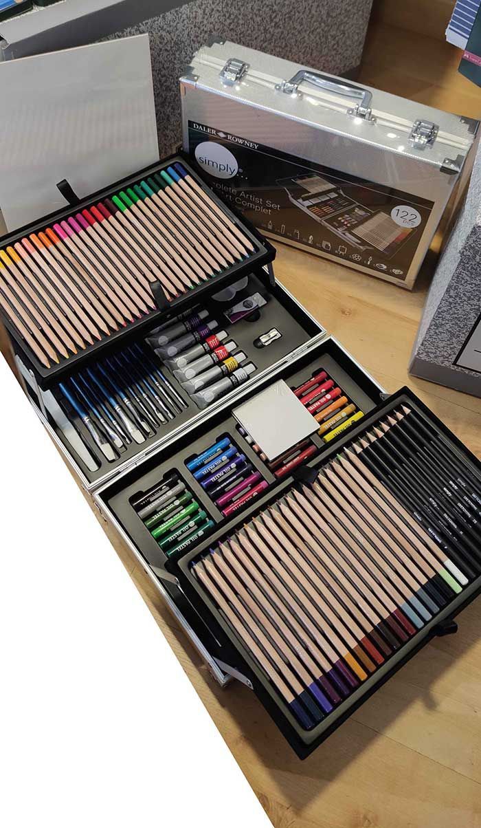 Estuche abierto para material artístico con lápices de colores, rotuladores y herramientas de dibujo organizados en compartimentos.