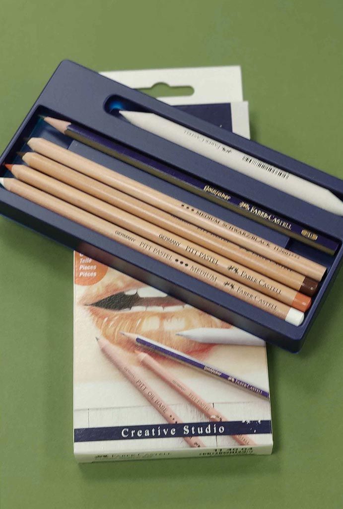 Estuche azul para lápices con varios lápices de madera colocados sobre una superficie verde.