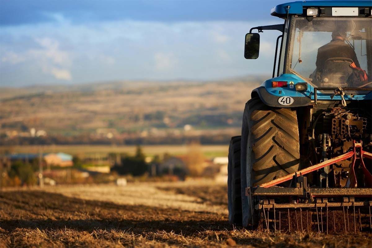 Tractor azul arando un campo, con un paisaje rural distante al fondo.