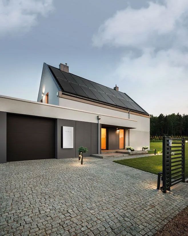 Casa con paneles solares en el techo, entrada para vehículos y camino iluminado al anochecer.