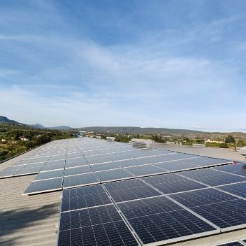 Paneles solares instalados en un tejado bajo un cielo azul, con un paisaje lejano visible.