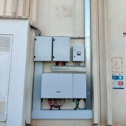 Componentes eléctricos de un panel solar montados en una pared de un edificio de color claro.