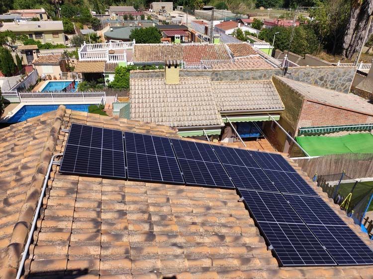 Paneles solares sobre un tejado con casas vecinales al fondo. Día soleado.