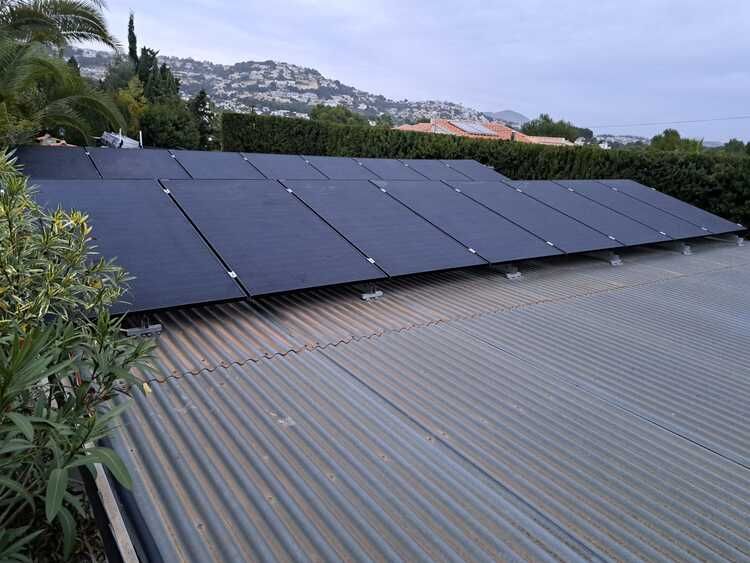 Paneles solares instalados en un techo de metal corrugado, con una vista de un pueblo en la ladera al fondo.