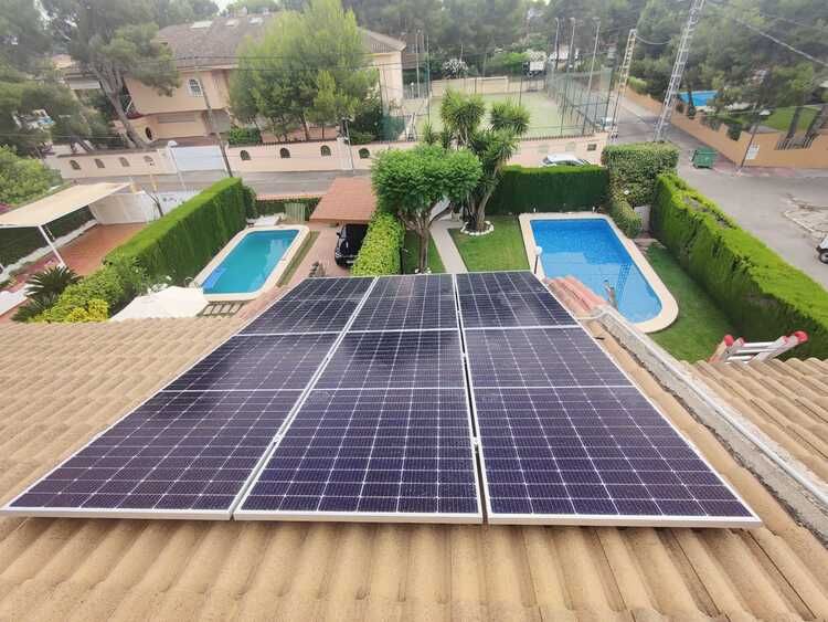 Paneles solares instalados en una azotea con vista a un patio trasero con dos piscinas y jardines.