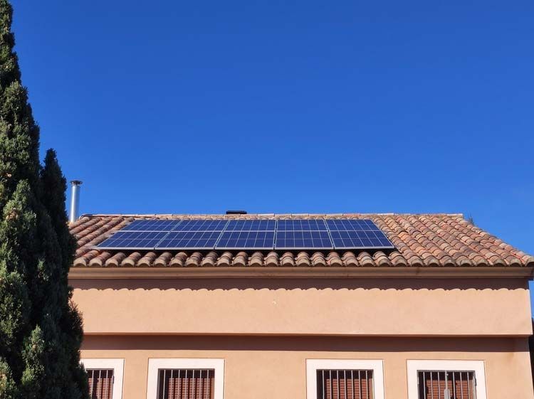 Paneles solares sobre un techo de tejas de terracota de un edificio beige contra un cielo azul claro.
