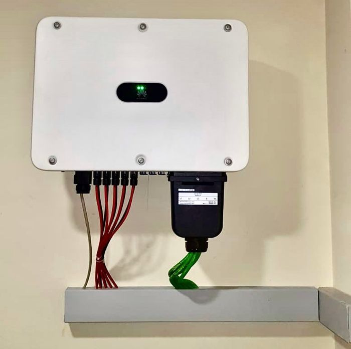 Inversor solar blanco y registrador de datos montado en la pared. Los cables rojo y negro se conectan al inversor y el cable verde al registrador de datos.