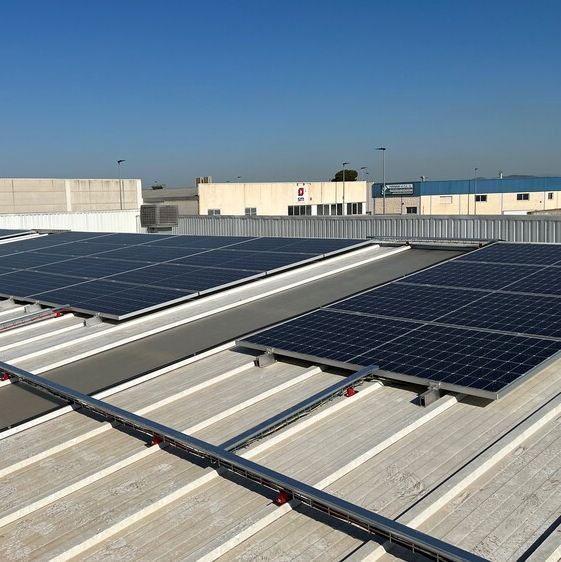 Paneles solares instalados en el techo de un edificio industrial blanco bajo un cielo azul claro.