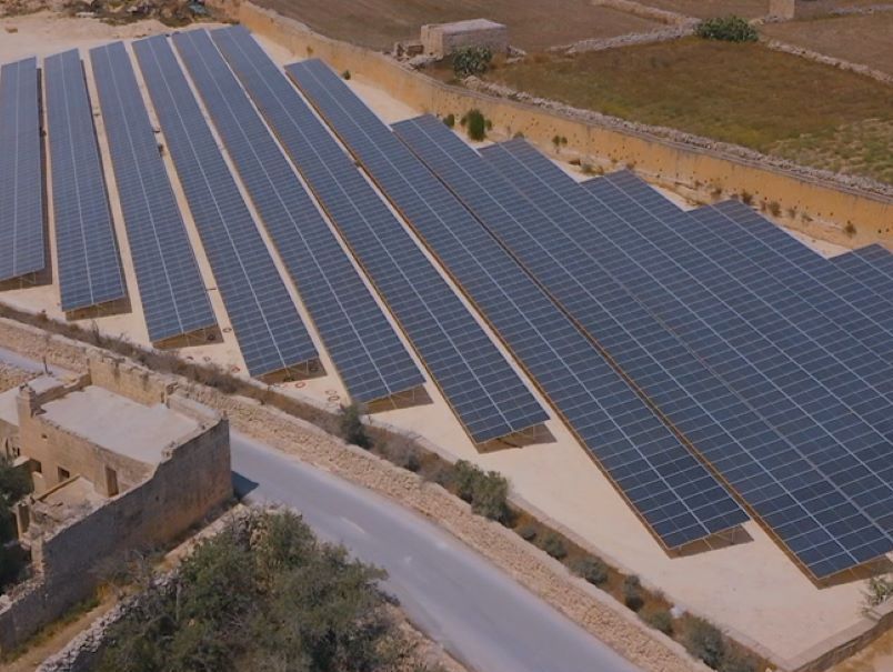 Vista aérea de un conjunto de paneles solares en un entorno rural con muros de piedra y una carretera.