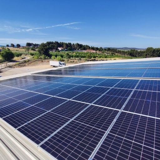 Paneles solares en un techo, bajo un cielo azul, con un camión blanco en la distancia.