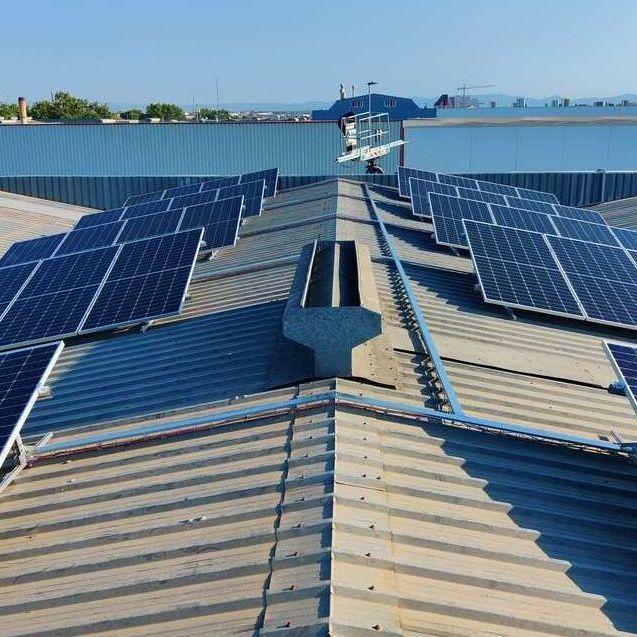 Paneles solares instalados en la azotea de un edificio comercial. Paneles azules, techo gris, día soleado.