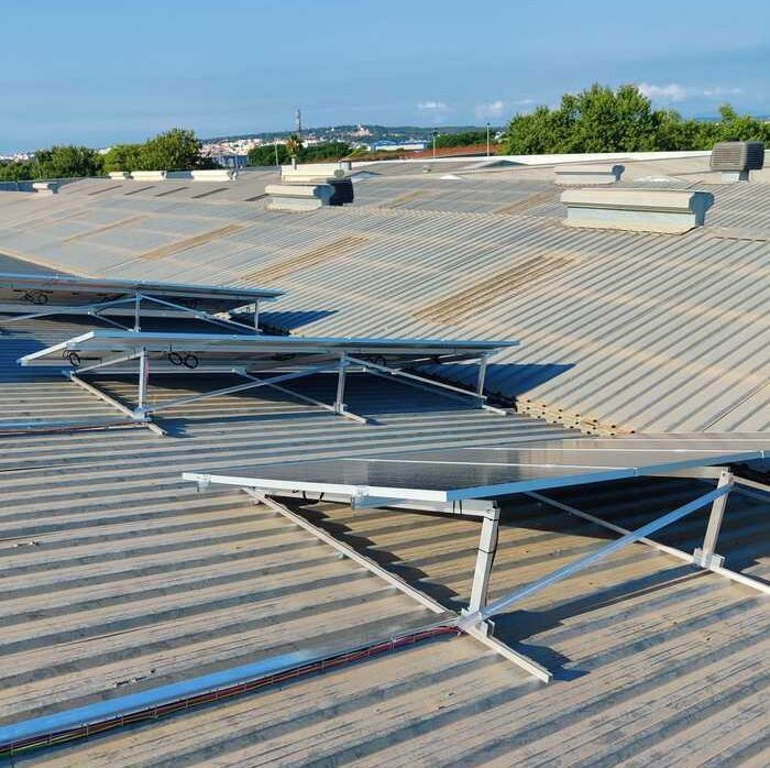 Paneles solares instalados en un techo de chapa ondulada. Día soleado, cielo azul y árboles al fondo.