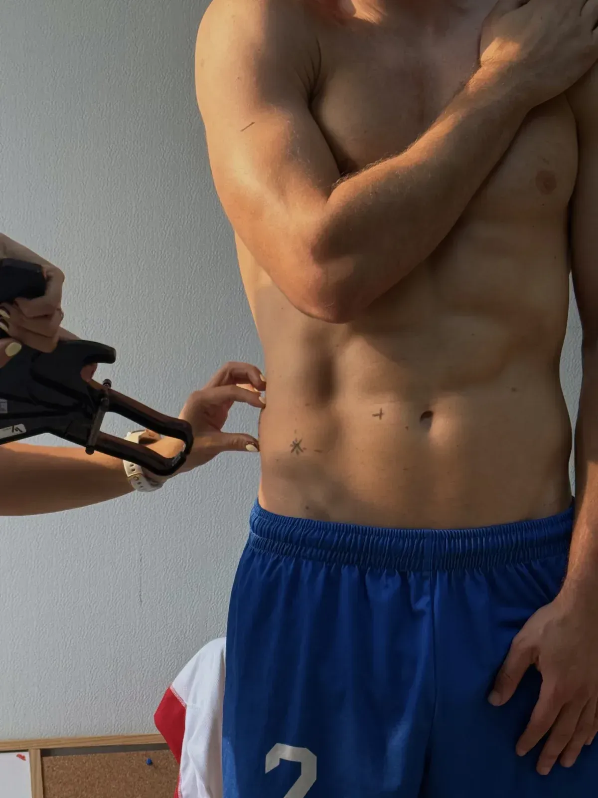 Primer plano de una persona sin camisa, vestida con pantalones cortos azules, a la que un pequeño maniquí