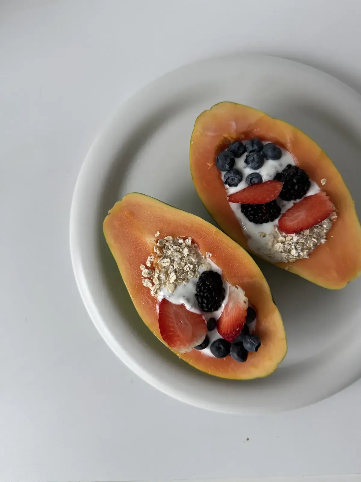 Dos papayas partidas por la mitad, cubiertas con bayas y granola en un plato blanco.