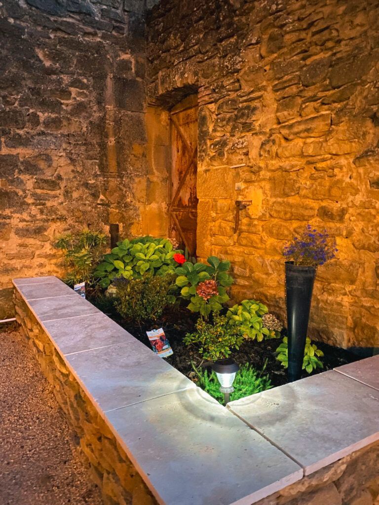 Coin de cour en pierre avec un petit parterre de fleurs et un éclairage