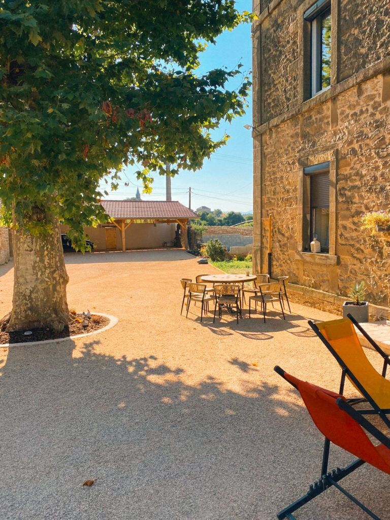 Cour ensoleillée gravillonnée jouxtant une maison en pierre