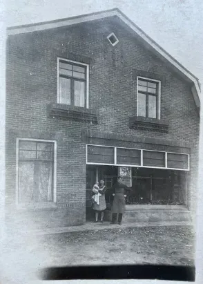 Ein Schwarzweißfoto eines Backsteingebäudes, vor dem zwei Personen stehen.