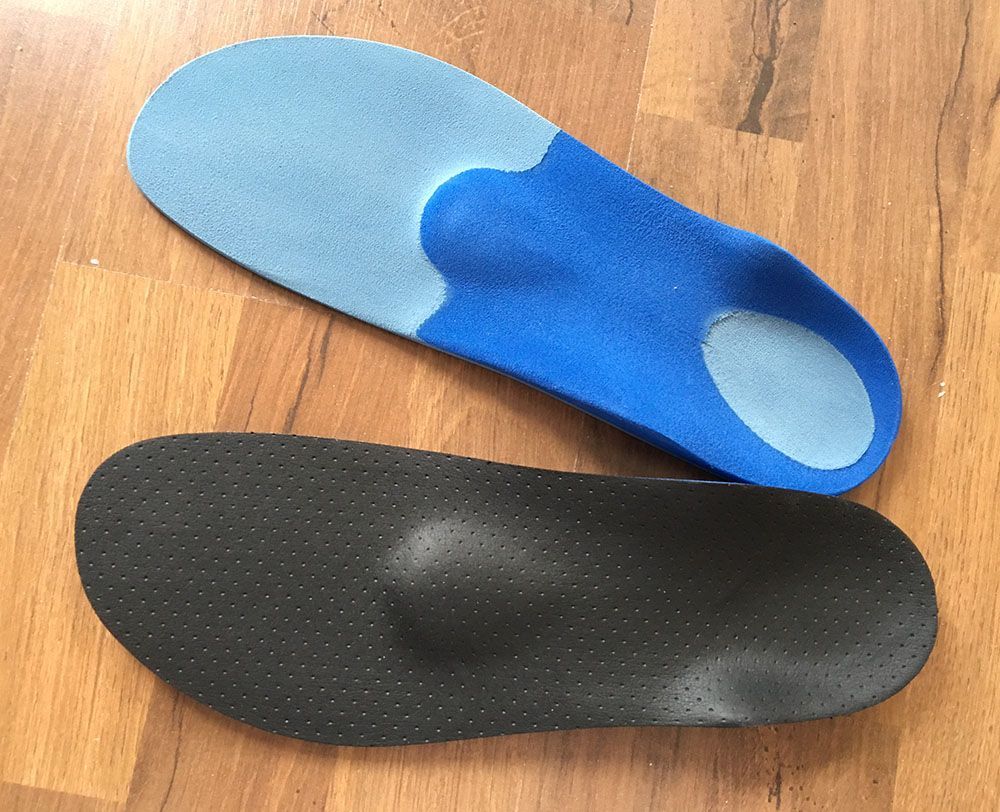 Ein Paar blaue und schwarze Einlegesohlen auf einem Holzboden